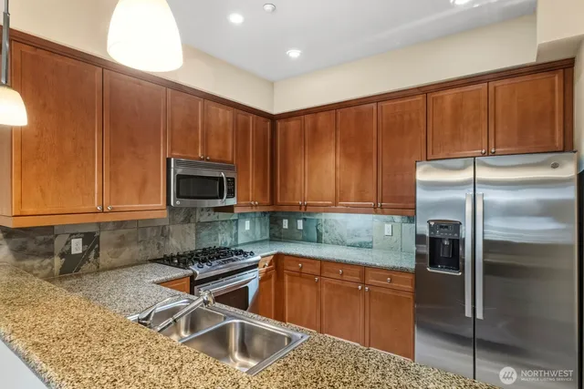 a kitchen with granite countertop stainless steel appliances a refrigerator a sink a stove a microwave cabinets and a counter top space