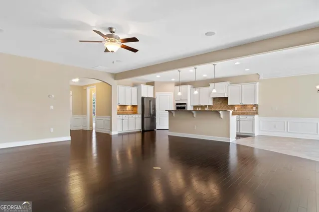 a view of an empty room with wooden floor and a kitchen