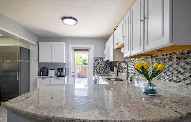 a living room with stainless steel appliances furniture a flat screen tv and a kitchen view