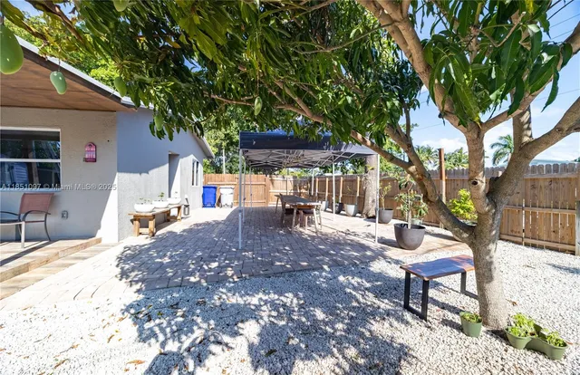 a view of a patio with a table and chairs under an umbrella with large trees