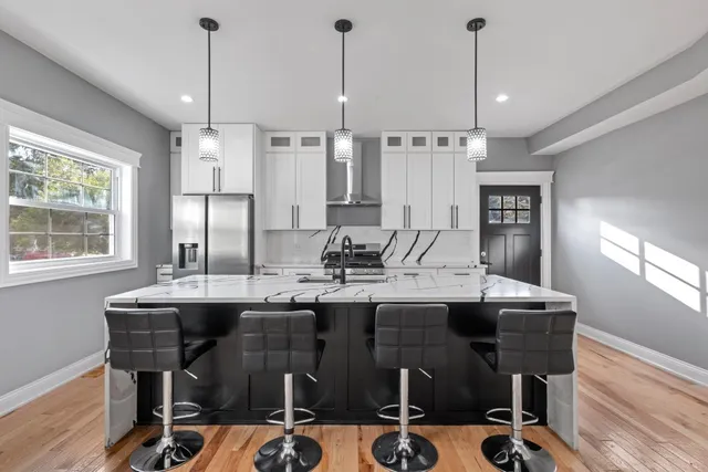 a kitchen with stainless steel appliances kitchen island granite countertop a stove a sink a refrigerator and white cabinets with wooden floor