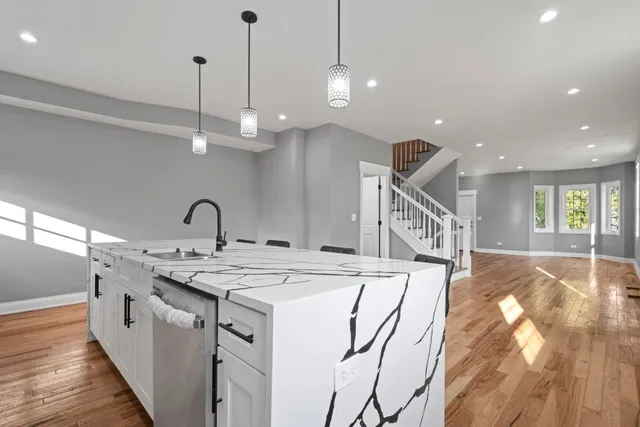 a large white kitchen with a large window a island wooden floor and stainless steel appliances
