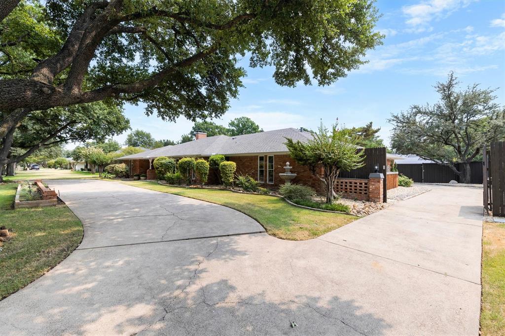 4446 Thunder Road Dallas, TX 75244 - Photo 6 of 36 Brick exterior, mature trees, and a concrete driveway with fence and electronic gate