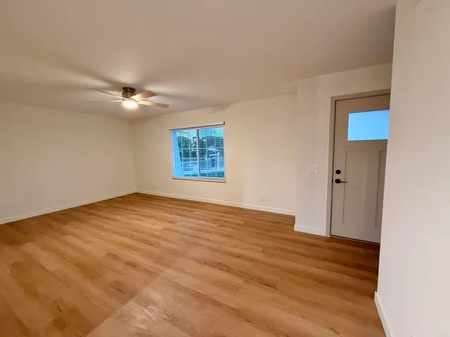 an empty room with wooden floor fan and windows