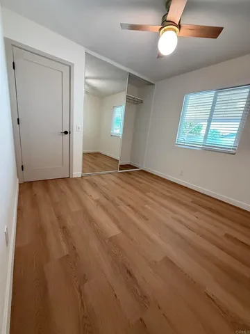 an empty room with wooden floor fan and windows