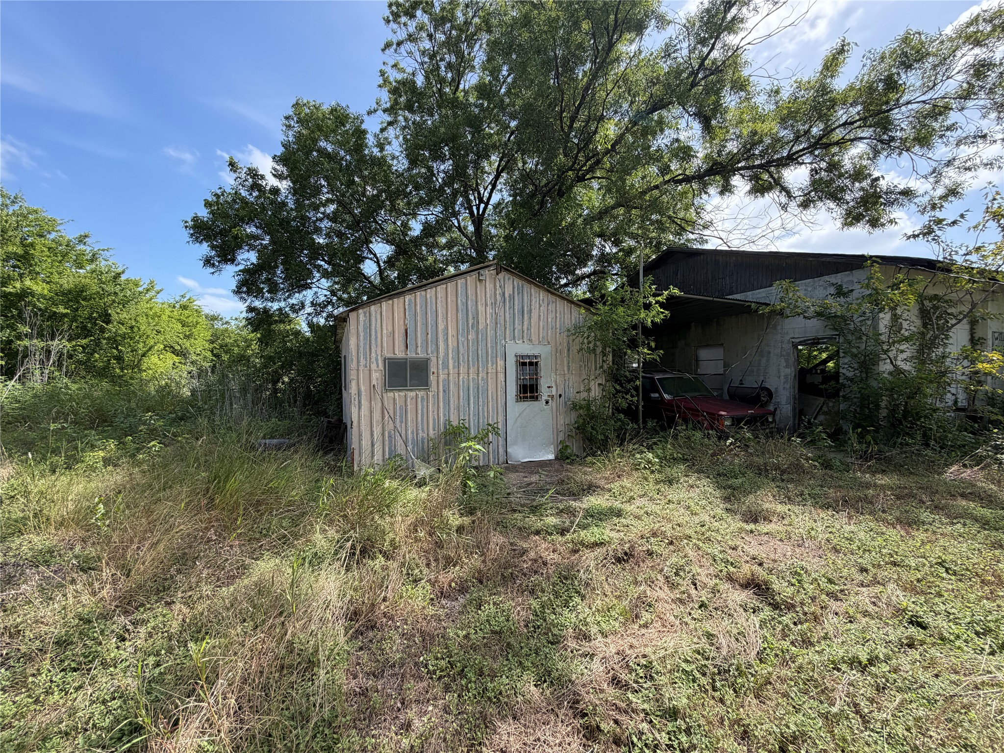 2501 Barnhardt Road Temple, TX 76502 - Photo 22 of 25 A rustic storage building and garage sit amidst overgrown foliage, offering potential for restoration.