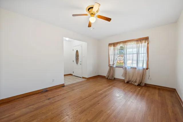 an empty room with wooden floor ceiling fan and windows