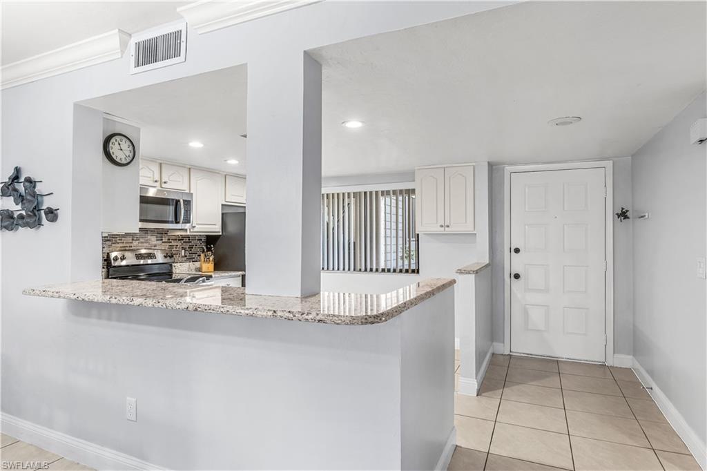 5841 Rattlesnake Hamm Road, Unit I101 Naples, FL 34113 - Photo 3 of 17 Kitchen with kitchen peninsula, appliances with stainless steel finishes, decorative backsplash, and white cabinetry