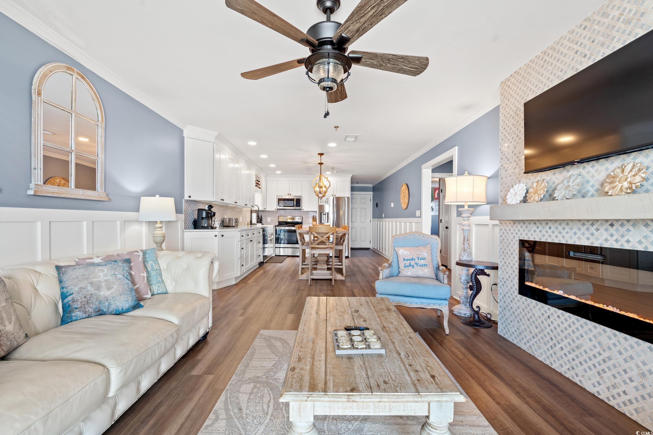 917 Ocean Boulevard South, Unit 304 Surfside Beach, SC 29575 - Photo 6 of 38 Living room with wainscoting, a tiled fireplace, crown molding, wood finished floors, and a ceiling fan