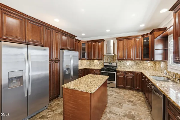 a kitchen with stainless steel appliances granite countertop a stove top oven a sink dishwasher and a refrigerator with wooden cabinets