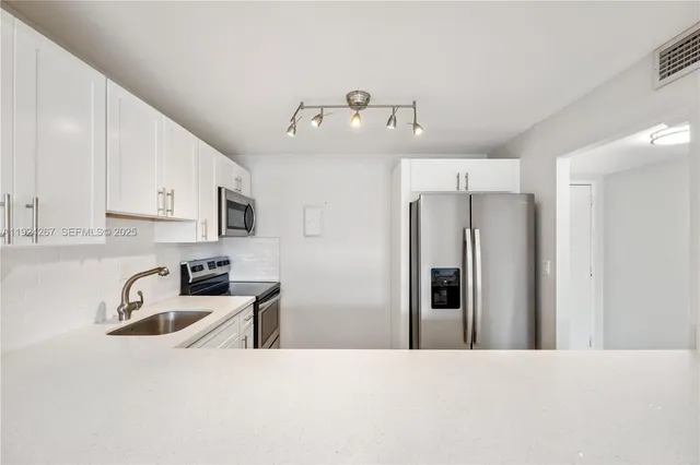 a kitchen with stainless steel appliances a refrigerator a sink a stove and white cabinets