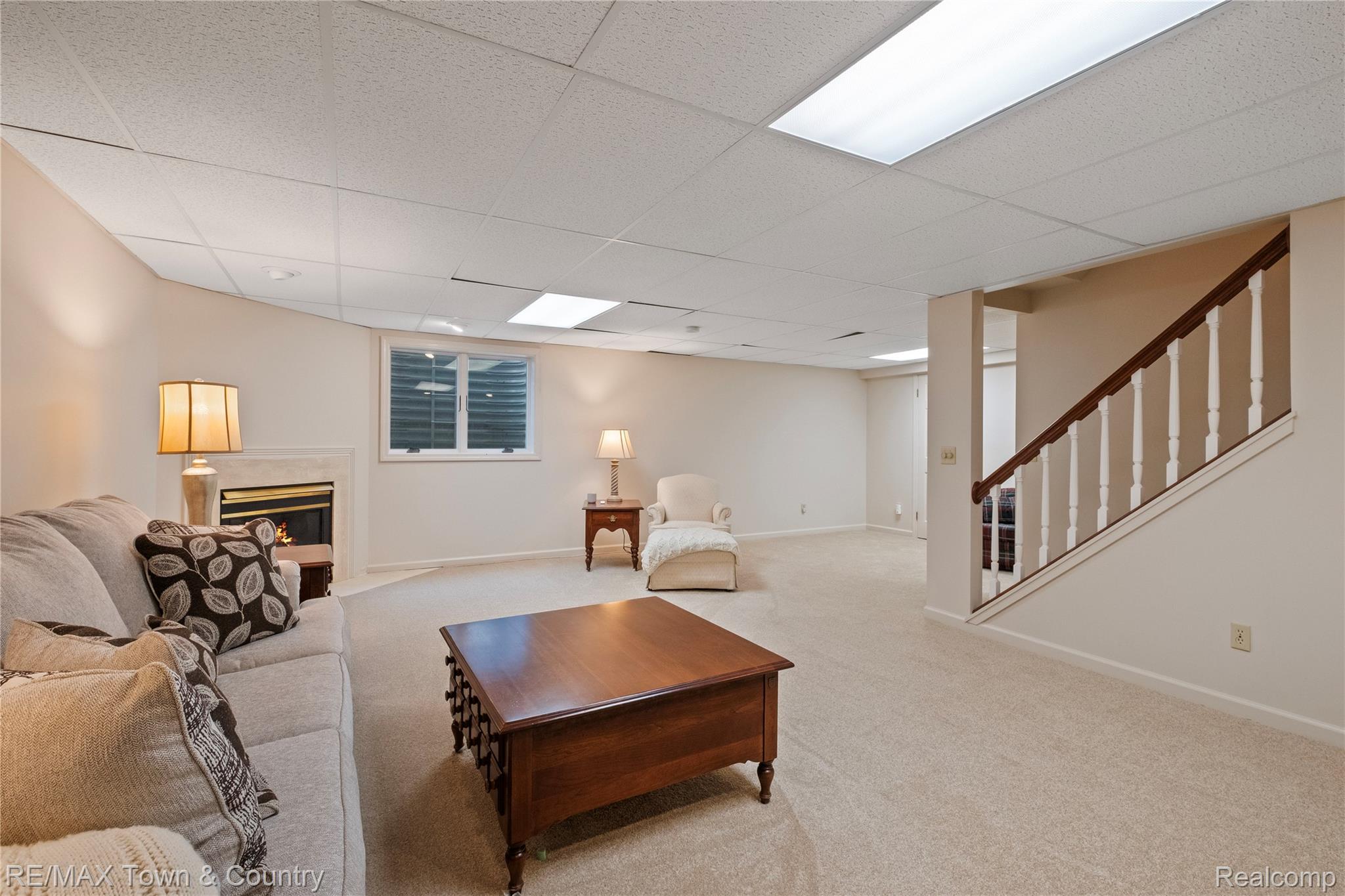 5464 North Seymour Road Flushing, MI 48433 - Photo 31 of 45 Carpeted floor, fireplace with stone surround, window with blinds, dropped ceiling with integrated lighting, and a staircase with wood handrail