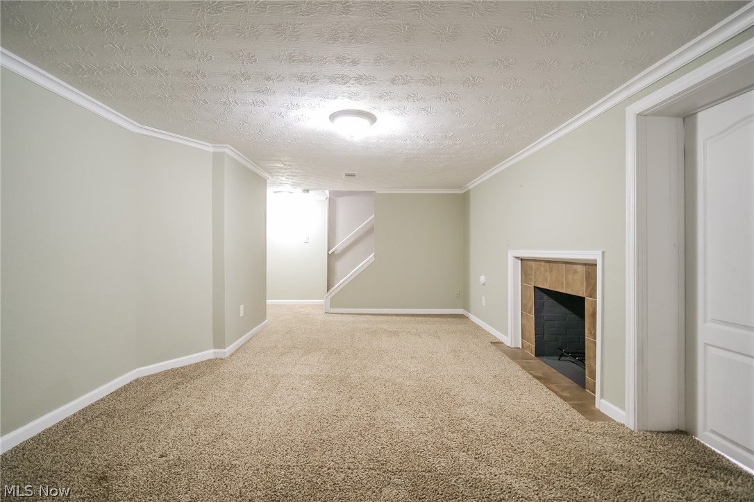 736 Quilliams Road Cleveland Heights, OH 44121 - Photo 5 of 20 Unfurnished living room featuring light colored carpet, a textured ceiling, a tile fireplace, and crown molding