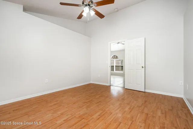 an empty room with wooden floor fan and windows
