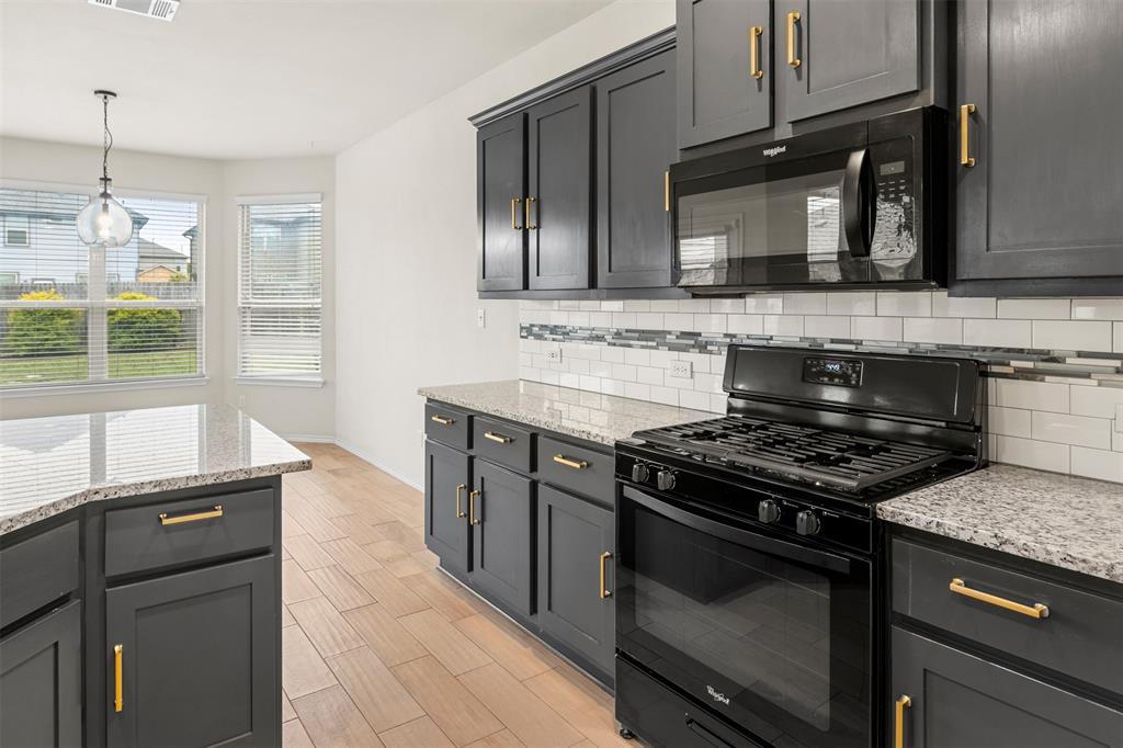 3560 Pauling Loop Round Rock, TX 78665 - Photo 11 of 28 Kitchen with black appliances, decorative backsplash, light stone countertops, wood finish floors, and pendant lighting