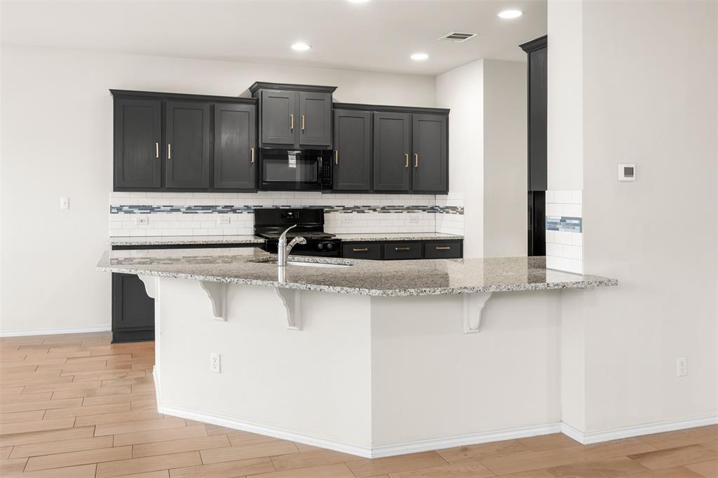 3560 Pauling Loop Round Rock, TX 78665 - Photo 13 of 28 Kitchen with a breakfast bar, a peninsula, backsplash, black appliances, and light wood-type flooring