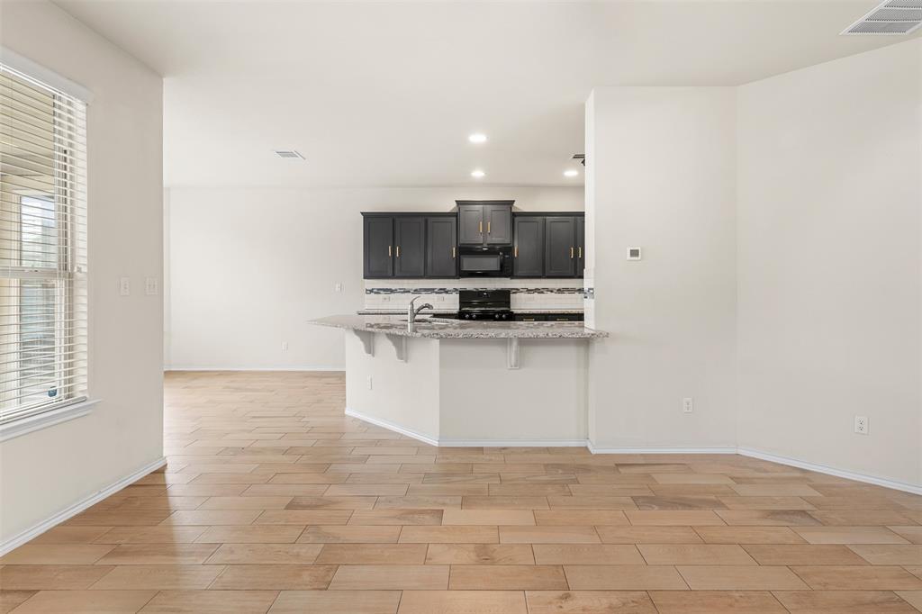 3560 Pauling Loop Round Rock, TX 78665 - Photo 15 of 28 Kitchen with a breakfast bar area, wood tiled floors, black appliances, light stone countertops, and a peninsula
