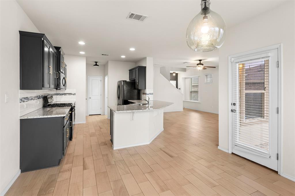 3560 Pauling Loop Round Rock, TX 78665 - Photo 3 of 28 Kitchen with dark cabinetry, light stone countertops, black appliances, a peninsula, and light wood finished floors
