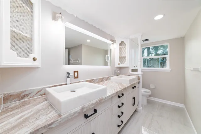 a spacious bathroom with a double vanity sink a mirror and a toilet