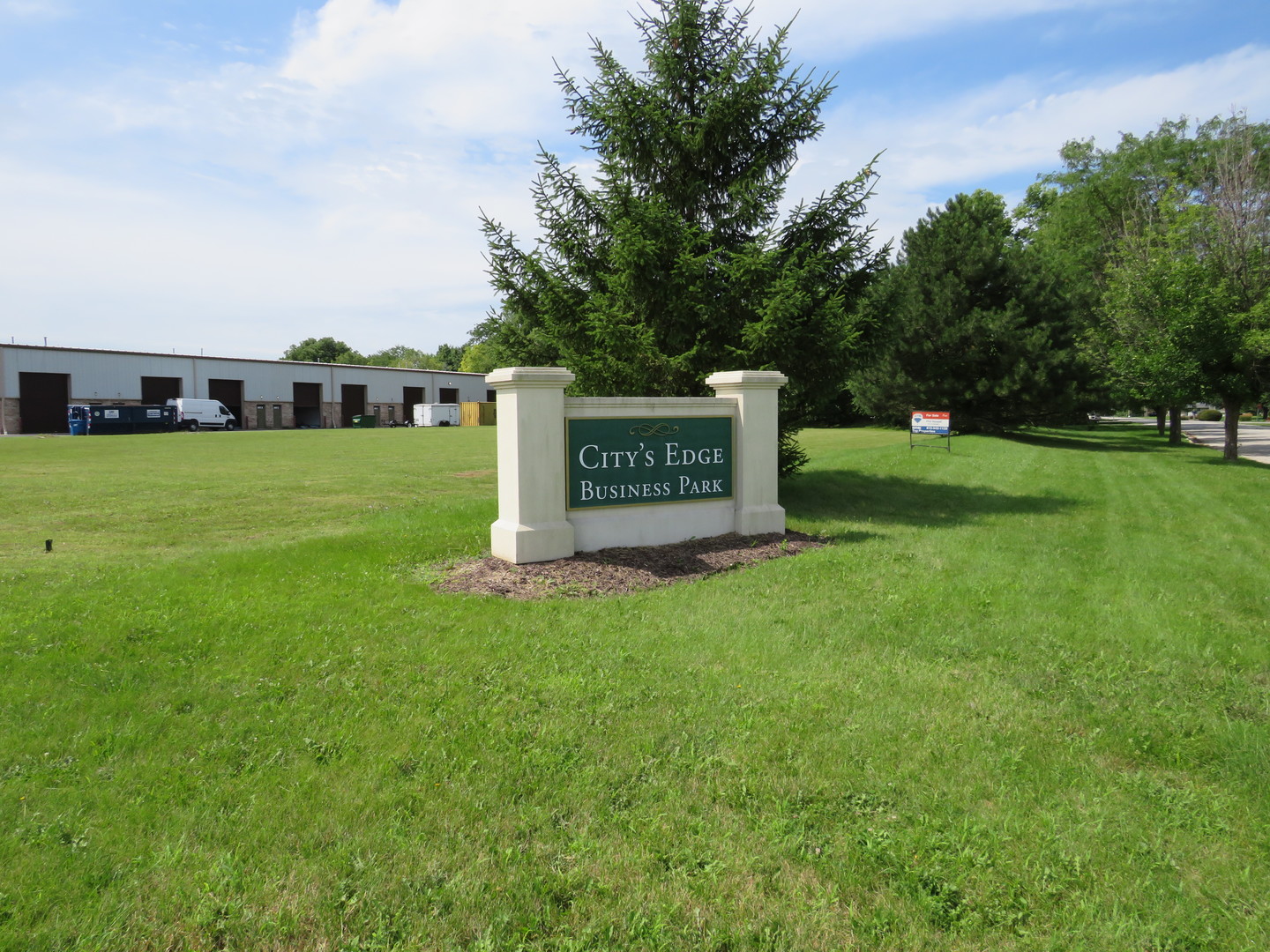 a view of a sign in front of a big yard with large trees