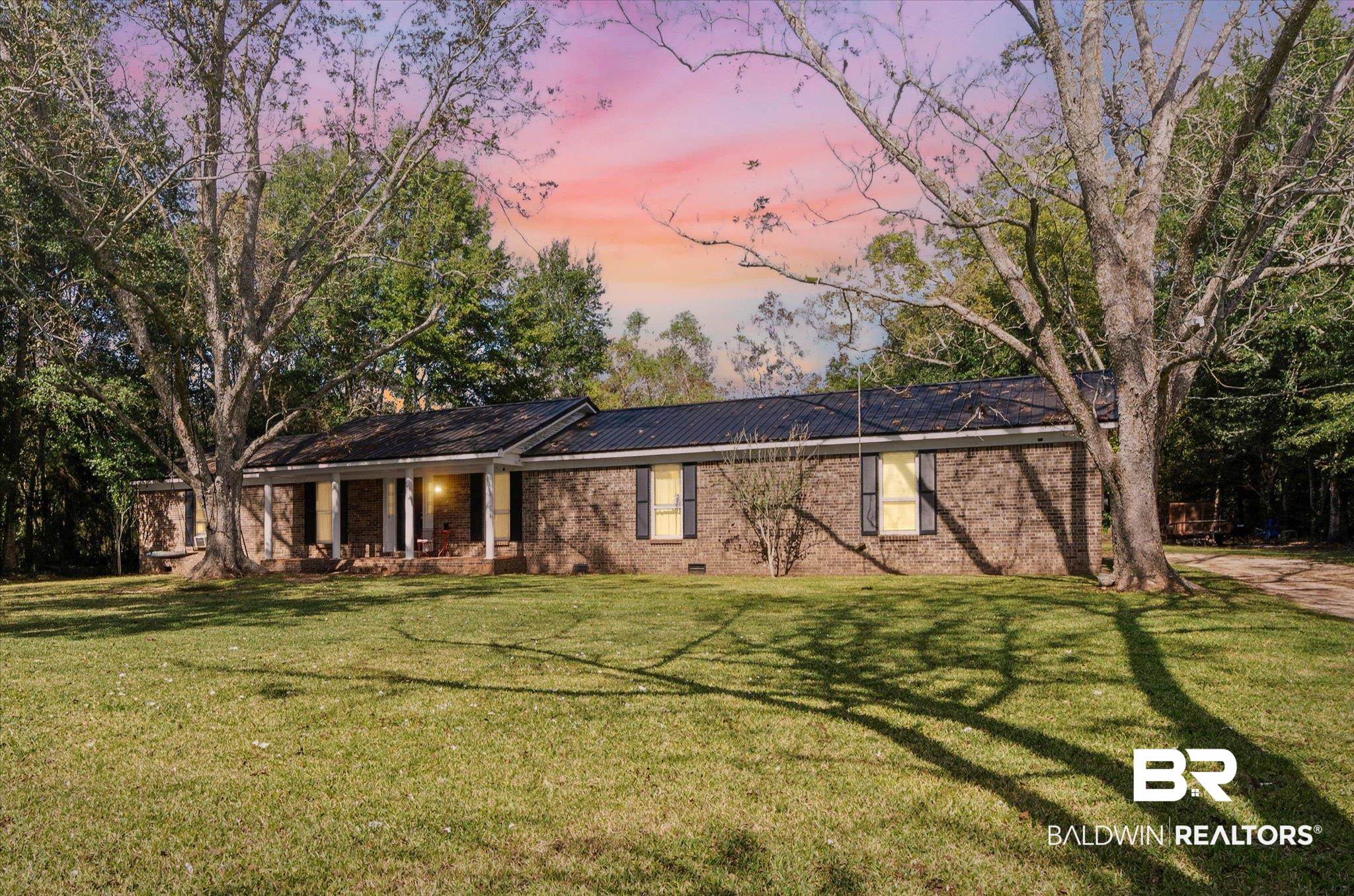 View of front of property with a yard, a metal roof, brick siding, a patio, and crawl space