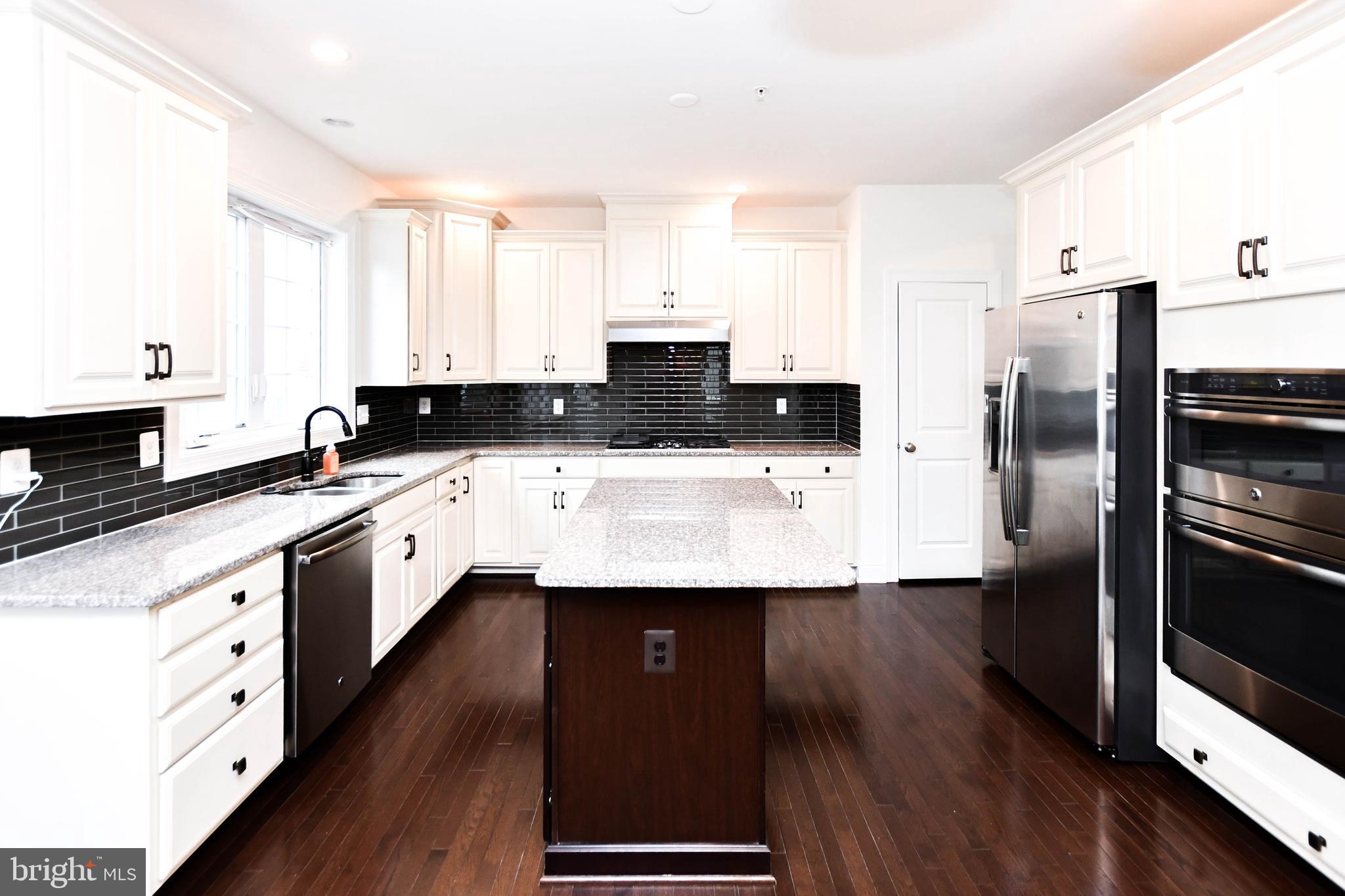 1610 Stream Valley Overlook Severn, MD 21144 - Photo 19 of 86 a kitchen with stainless steel appliances a sink dishwasher a refrigerator a stove and white cabinets with wooden floor