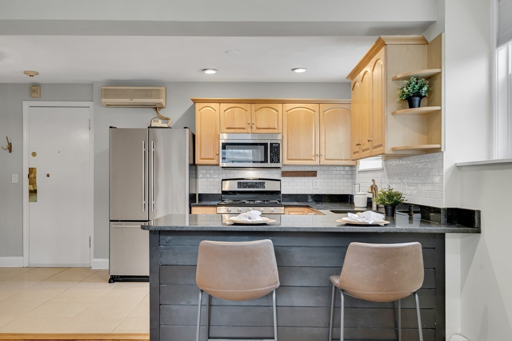 60 Charlesgate West, Unit BA Boston, MA 02215 - Photo 17 of 37 a kitchen with stainless steel appliances granite countertop a refrigerator a sink a stove a dining table and chairs with wooden floor