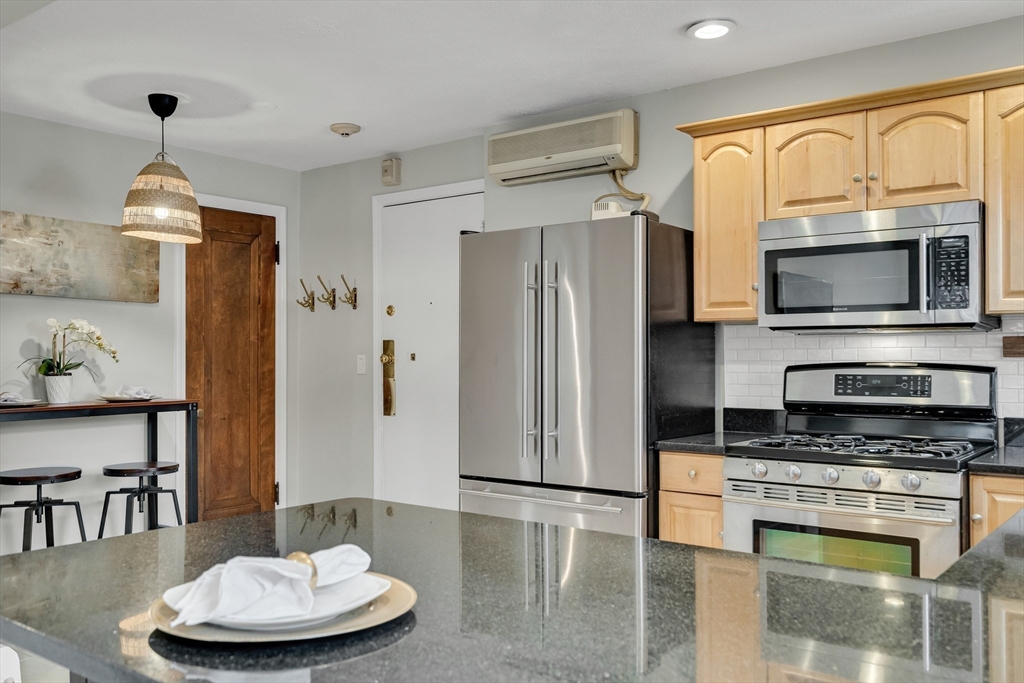 60 Charlesgate West, Unit BA Boston, MA 02215 - Photo 19 of 37 a kitchen with stainless steel appliances granite countertop a refrigerator a stove top oven a dining table and chairs with wooden floor