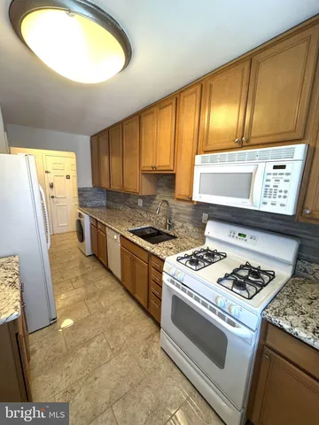a kitchen with granite countertop stainless steel appliances a stove a sink a refrigerator wooden floor and cabinets