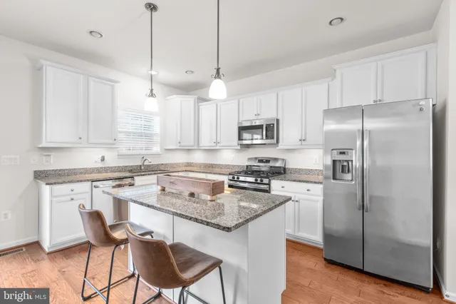 a kitchen with stainless steel appliances granite countertop a sink a stove a refrigerator and white cabinets