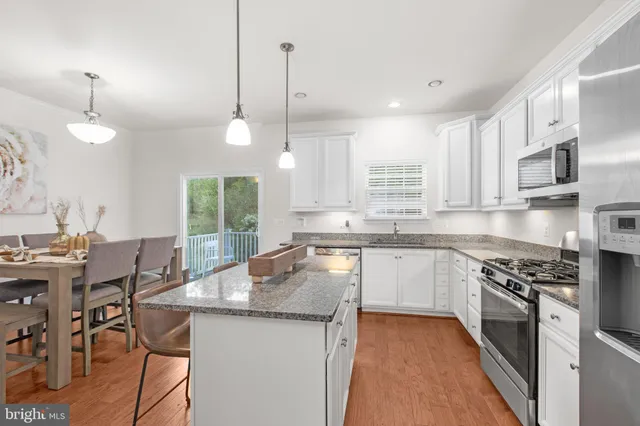 a kitchen with stainless steel appliances granite countertop a stove top oven a sink a dining table and chairs with wooden floor