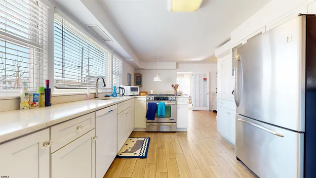 a kitchen with stainless steel appliances a refrigerator a sink a stove and white cabinets with wooden floor