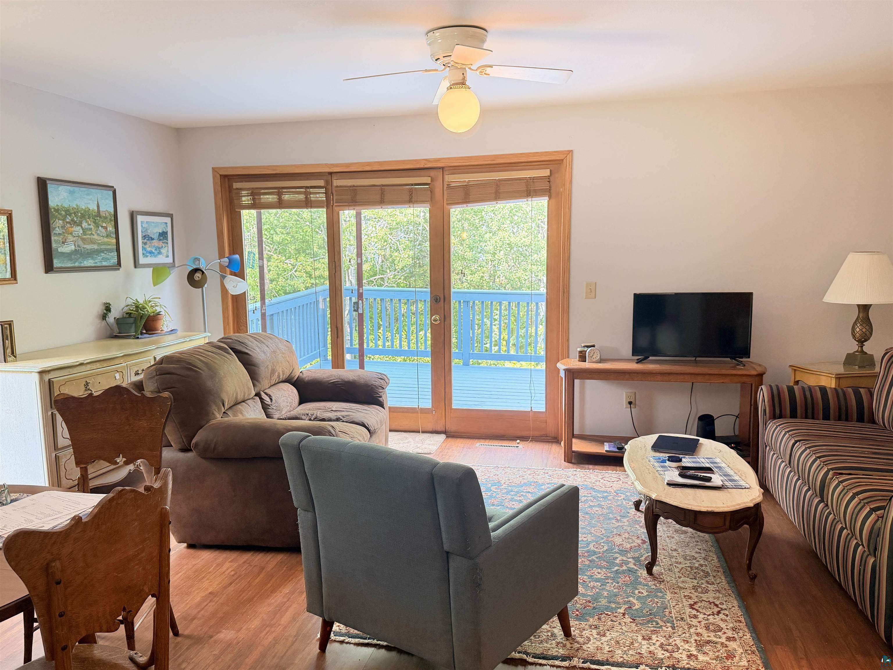 Wood-finish flooring, ceiling fan, and sliding glass door leading to an exterior deck with blue railings