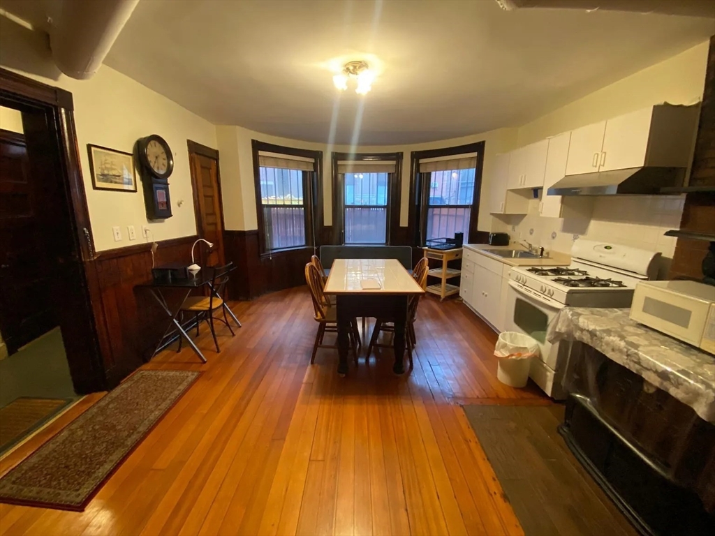 a living room with dining room furniture wooden floor and a kitchen view