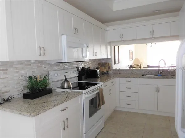 a kitchen with granite countertop a sink stainless steel appliances white cabinets and a window