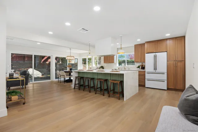 a kitchen with stainless steel appliances kitchen island granite countertop a refrigerator a stove a sink a dining table and chairs with wooden floor