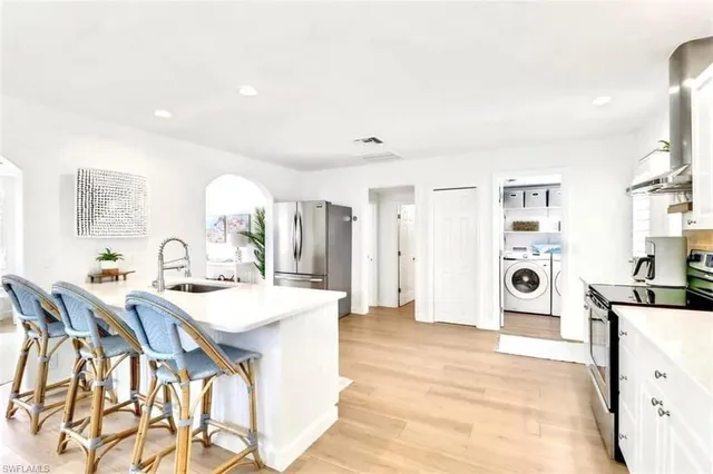 a large white kitchen with a refrigerator a stove a sink dishwasher with a dining table and chairs