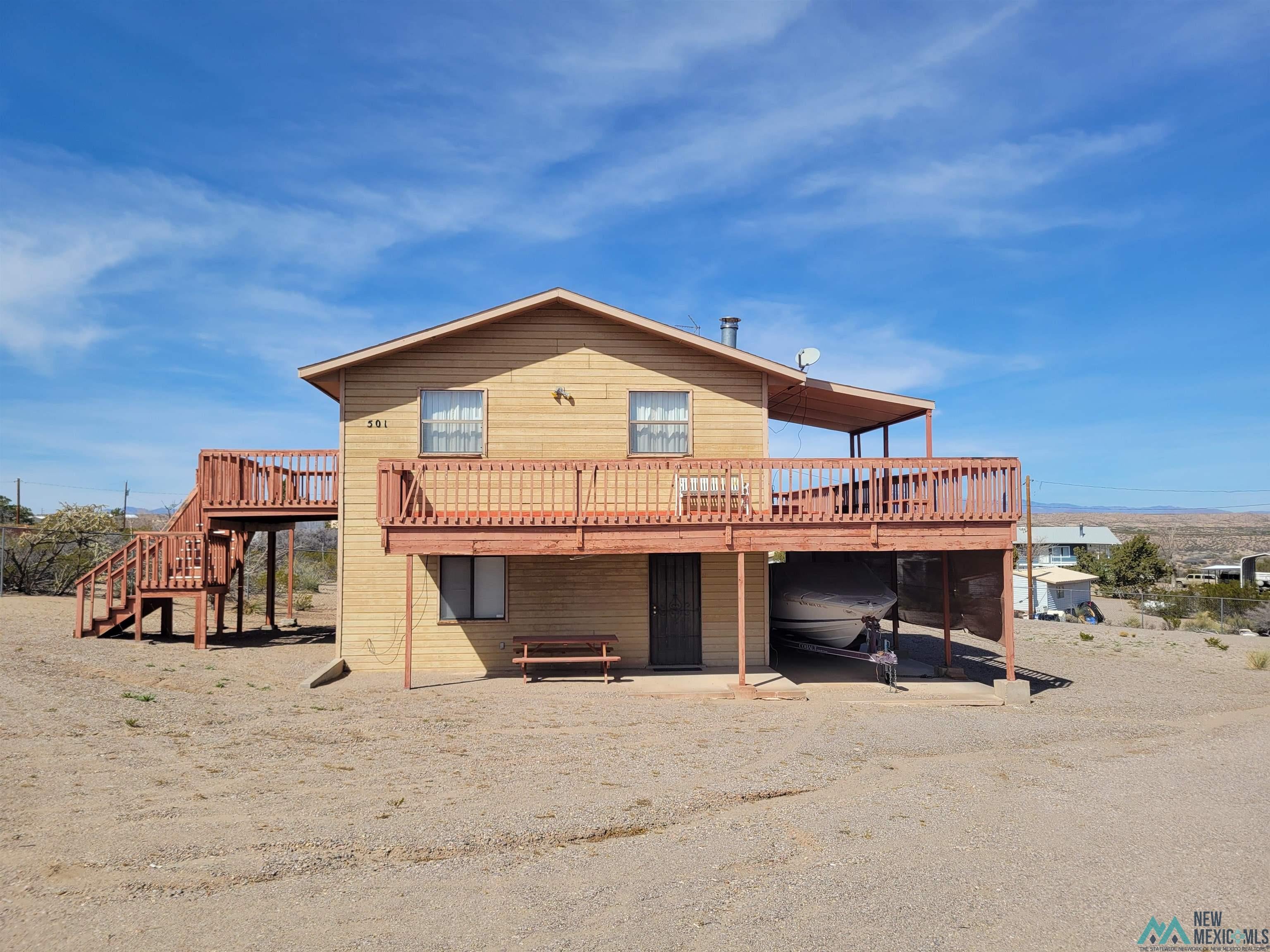 501 Springland Boulevard Elephant Butte, NM 87935 - Photo 26 of 38 Two-story residence featuring light-colored horizontal siding and a prominent wrap-around wood deck with reddish-brown railings