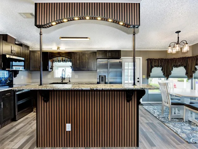 a kitchen with stainless steel appliances granite countertop a sink wooden cabinets and a wooden floor