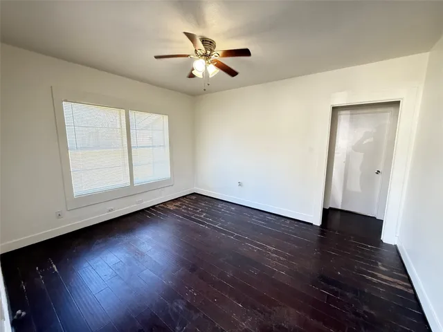 an empty room with wooden floor chandelier fan and windows