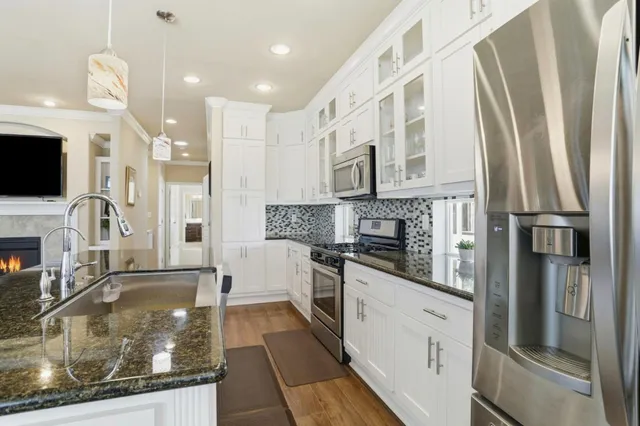 a kitchen with stainless steel appliances granite countertop a refrigerator a oven and white cabinets with wooden floor