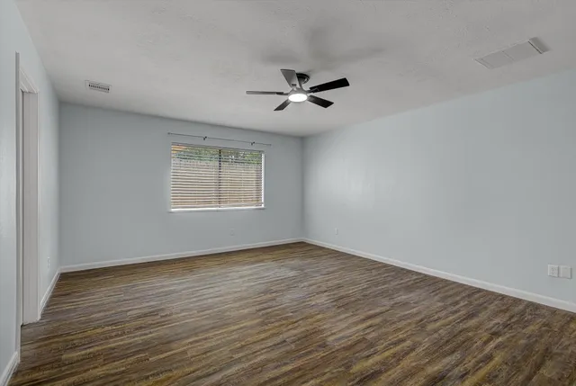 an empty room with wooden floor ceiling fan and windows