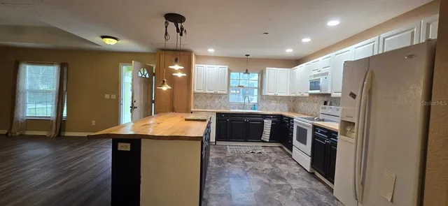 a kitchen with stainless steel appliances granite countertop a refrigerator a sink dishwasher a stove and a dining table with wooden floor