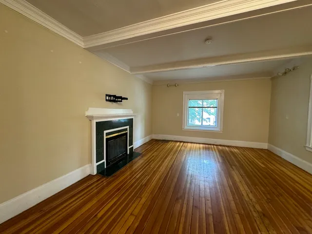 a view of an empty room with wooden floor fireplace and a window