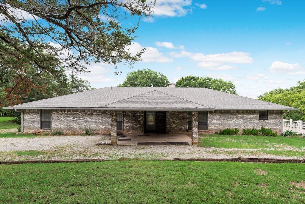 Grey brick exterior featuring a covered patio, multiple windows, and a dark shingle roof