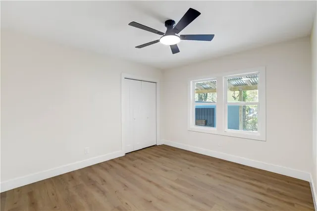 an empty room with wooden floor ceiling fan and windows