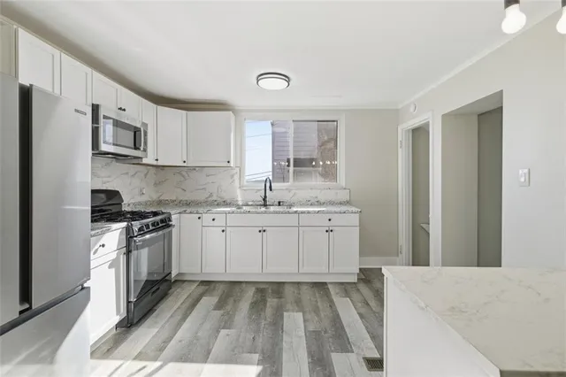 a kitchen with granite countertop a sink stainless steel appliances and white cabinets