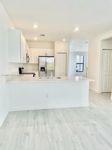 a view of a kitchen with kitchen island a sink stainless steel appliances and white cabinets