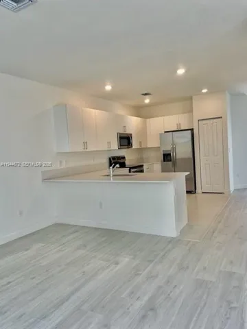 a view of kitchen with stainless steel appliances refrigerator oven a microwave with white cabinets and wooden floor