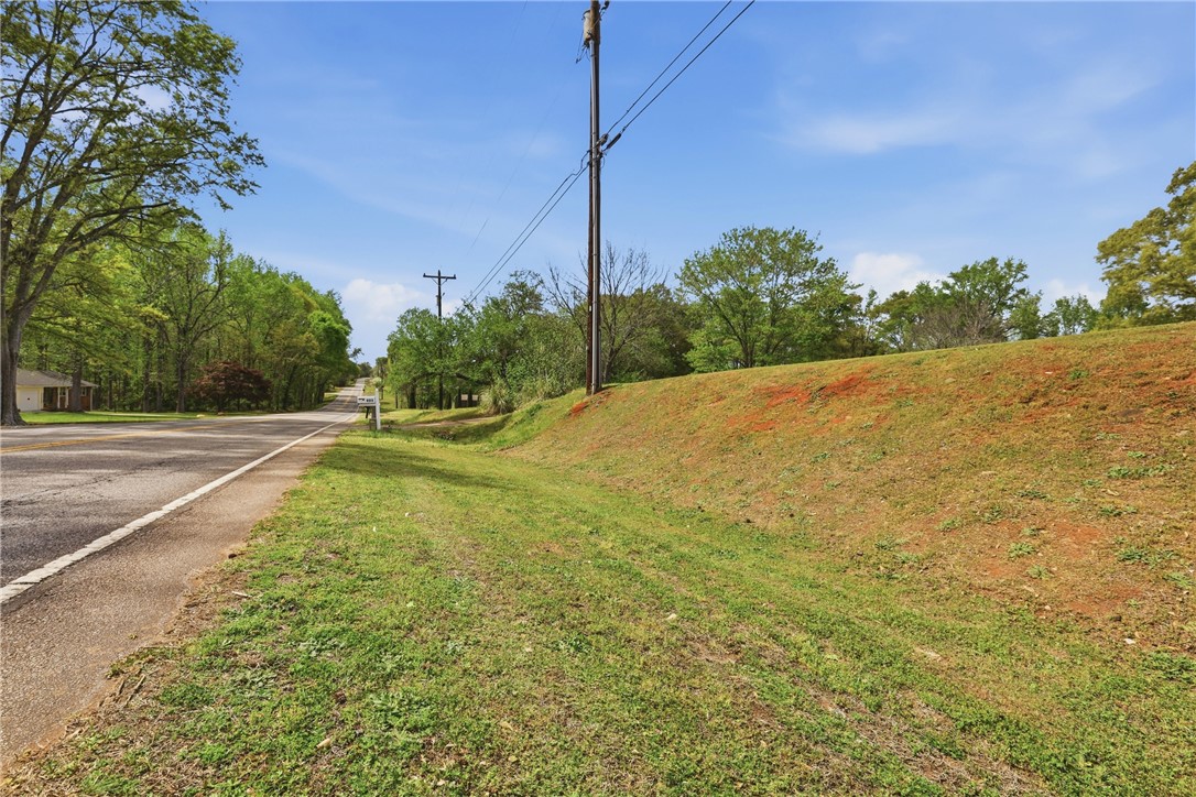 904 New Prospect Church Road Anderson, SC 29625 - Photo 28 of 31 A verdant roadside view showcases an open lot with mature trees under a clear sky.